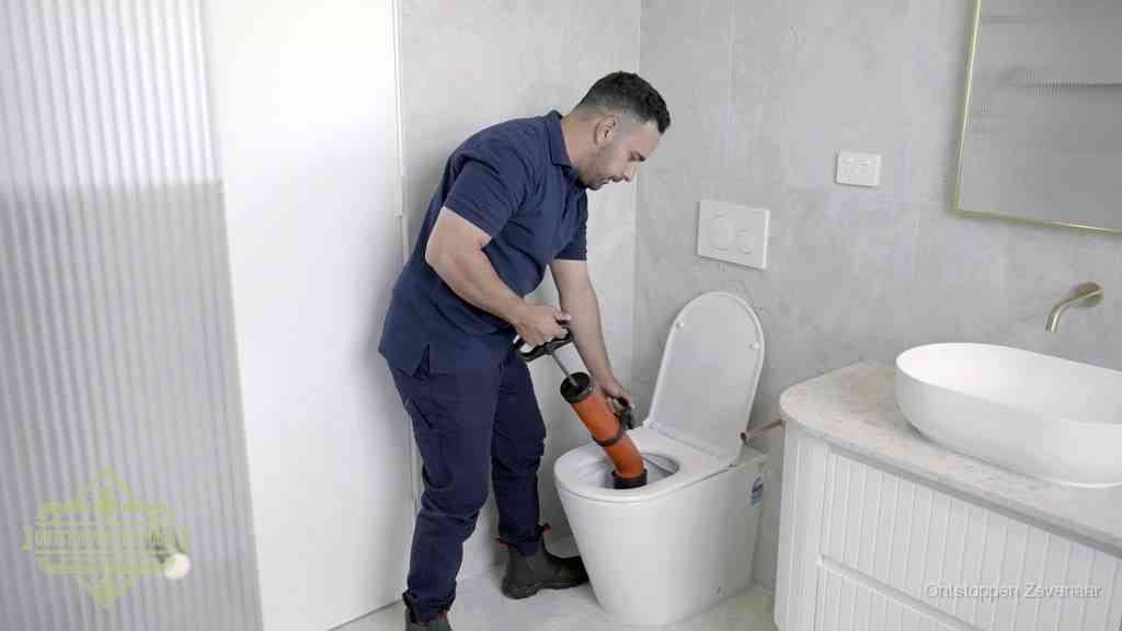 Een monteur buigt over een wandcloset en duwt met de hand een persluchtontstopper in de toiletpot om de verstopping handmatig los te maken in Zevenaar