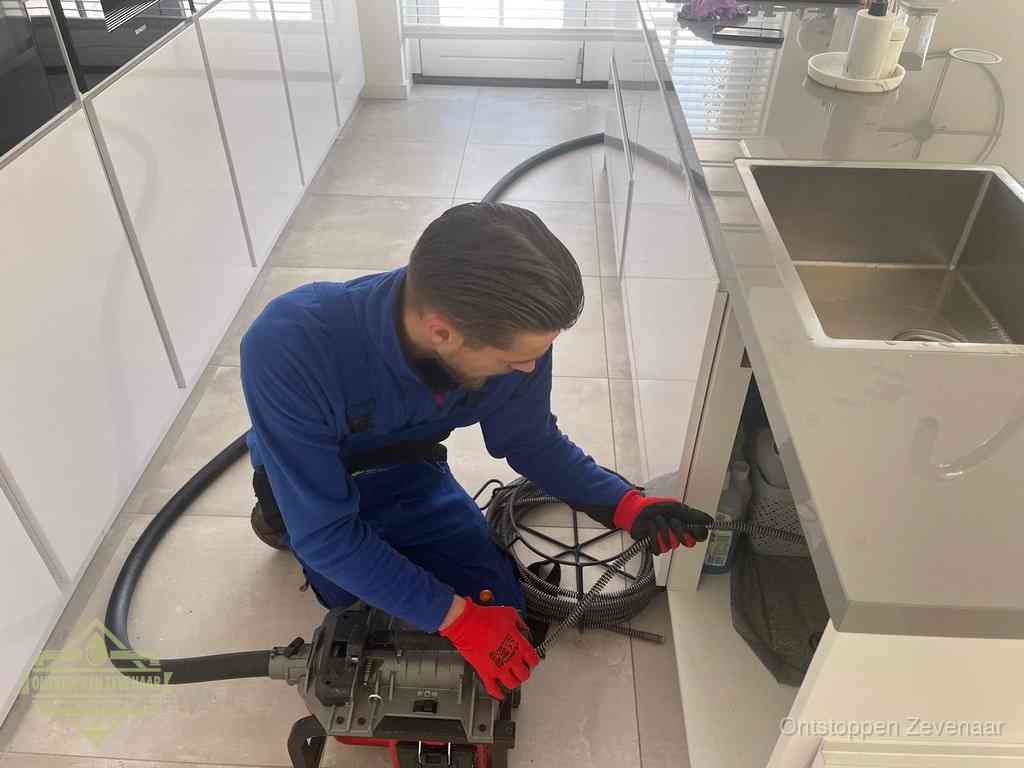 Een monteur ontstopt de keukenafvoer onder de spoelbak met een elektrische veermachine in Zevenaar