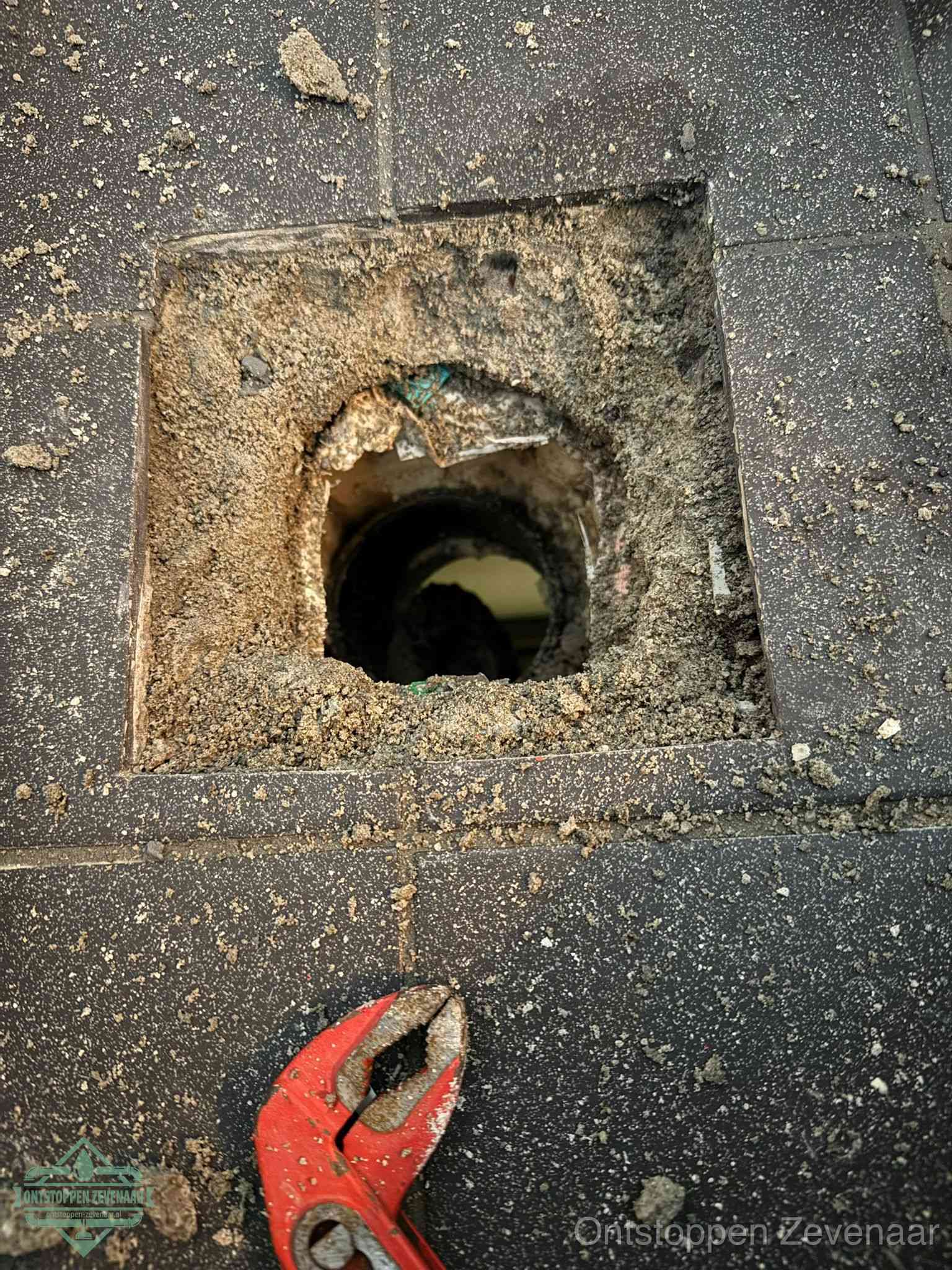 Een geopend rioolputje in een betontegelvloer met losgemaakt rooster en een zichtbare ronde afvoerbuis, het achterhalen waar de afvoerverstopping zit in Zevenaar