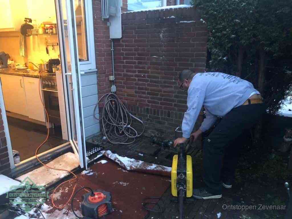 Een monteur werkt buiten bij een open riool-/grondput met een elektrische ontstoppingsmachine om een verborgen afvoerprobleem op te sporen in Zevenaar