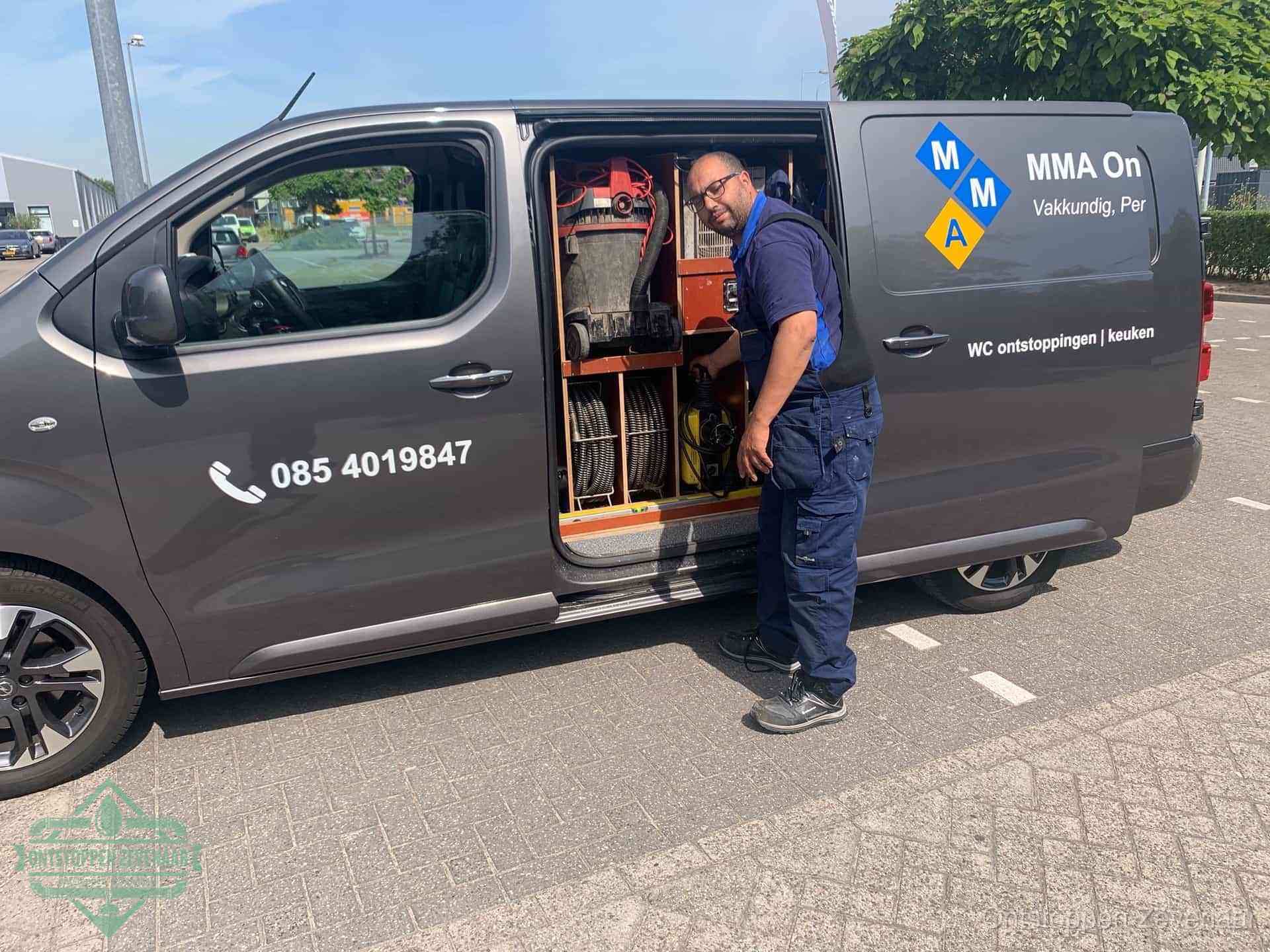 Een monteur bij de open schuifdeur van zijn bedrijfsbus op een parkeerplaats, klaar om de oorzaak van terugkerende afvoerverstoppingen aan te pakken in Zevenaar