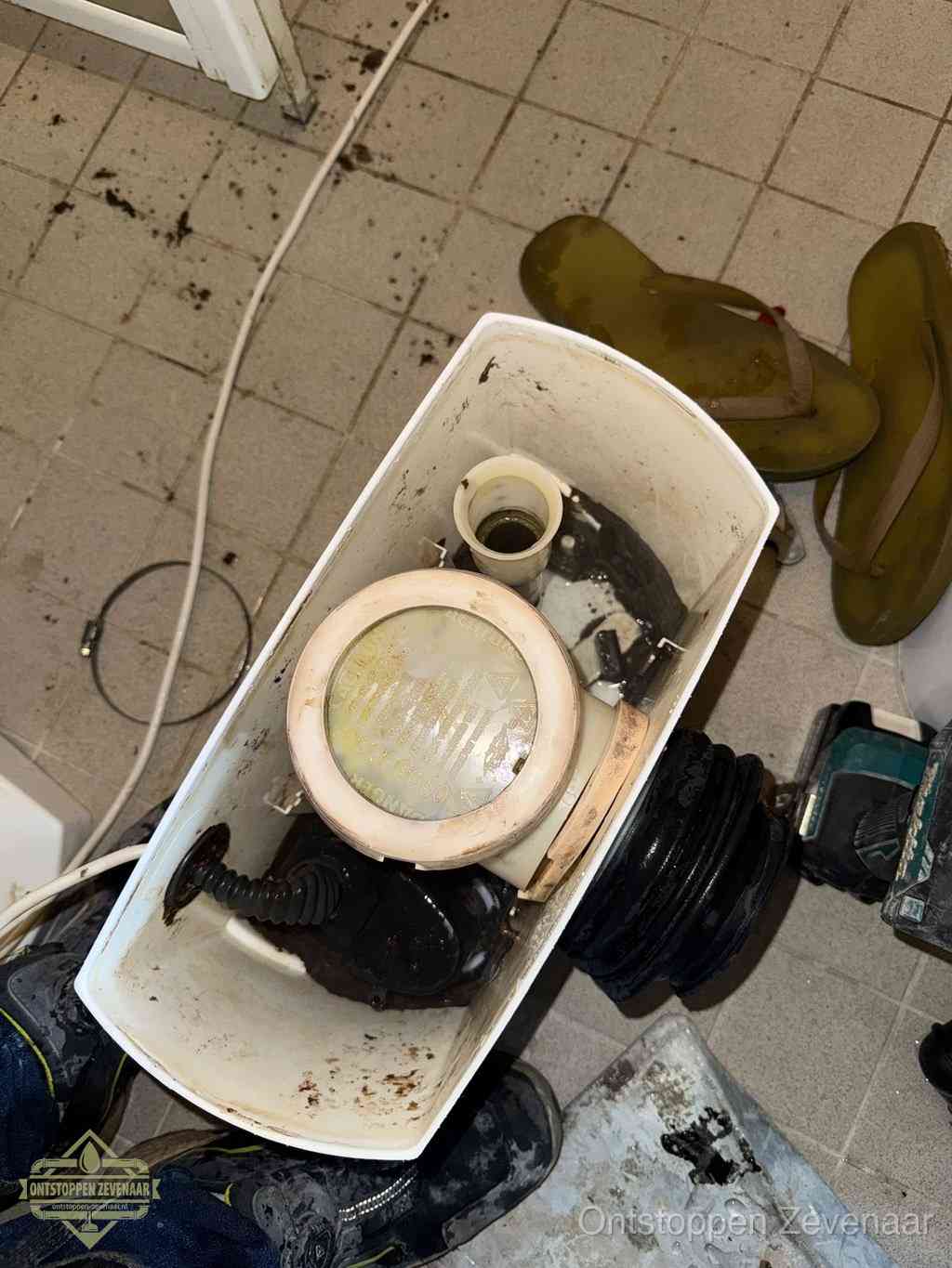 Een gedemonteerde toiletpot op de vloer met ontstoppingsveer en gereedschap ernaast, het verwijderen van een vastzittend voorwerp uit de wc in Zevenaar