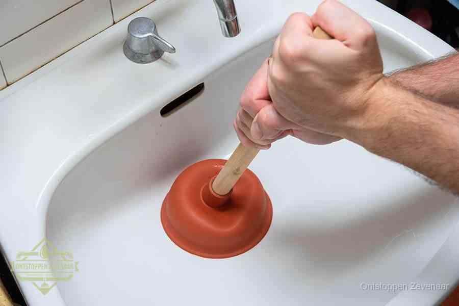 Twee handen gebruiken een rode rubberen plopper op een sanitair-afvoer om het toilet te ontstoppen in Zevenaar