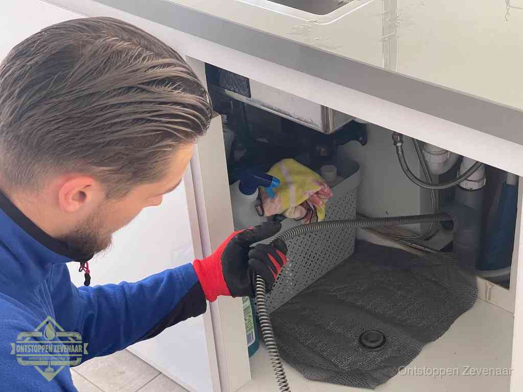 Een monteur voert een flexibele ontstoppingsveer in de afvoer om een verstopping voorbij de bocht van het toilet te bereiken in Zevenaar